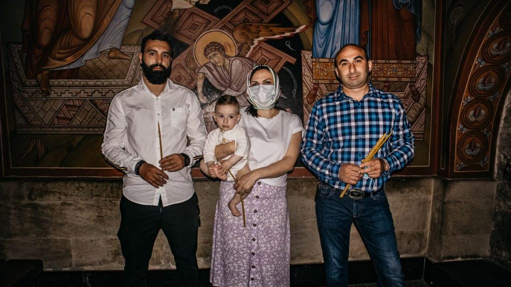 A family poses for a photo during a baptism ceremony in a church, highlighting religious tradition.